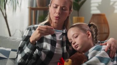 Ev hekimliği konseptinde beyaz bir aile. Anne kızına sarılıyor. Sıcaklığı ölçüyor.