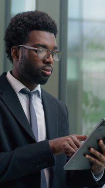 Ofisteki düşünceli Afrikalı Amerikalı işadamı pencereden dışarı bakan dijital tablet kullanarak odaklanmış iş adamı teknolojiyi kullanarak strateji planlamayı profesyonel iş olarak düşünüyor.