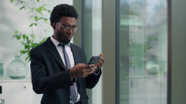 Kafası karışmış afro-amerikan erkek işadamı ofiste akıllı telefon okuyarak kötü haber okuyor cep telefonuyla yapılan şok sohbetinin hayal kırıklığına uğrattığını söylüyor.