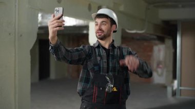 İnşaat mühendisi, beyaz adam video görüntülü konuşma, cep telefonu konferansı. İnşaat ustası mimar, akıllı telefon dostu, güler yüzlü apartman yenileme hakkında konuşuyor.