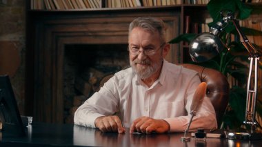 Kendinden emin, yaşlı, beyaz, olgun bir erkek kamera önünde el ele tutuşmuş ofis işadamı yakışıklı, yaşlı çalışan portresi liderinin içindeki iş adamına bakıyor.