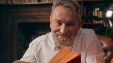 Kendinden emin, yaşlı, beyaz, olgun bir erkek kamera önünde el ele tutuşmuş ofis işadamı yakışıklı, yaşlı çalışan portresi liderinin içindeki iş adamına bakıyor.