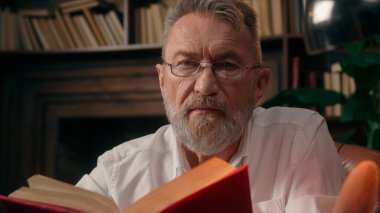 Kendinden emin, yaşlı, beyaz, olgun bir erkek kamera önünde el ele tutuşmuş ofis işadamı yakışıklı, yaşlı çalışan portresi liderinin içindeki iş adamına bakıyor.