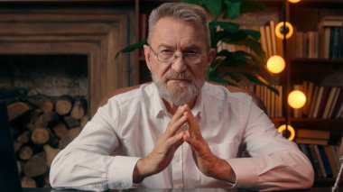 Kendinden emin, yaşlı, beyaz, olgun bir erkek kamera önünde el ele tutuşmuş ofis işadamı yakışıklı, yaşlı çalışan portresi liderinin içindeki iş adamına bakıyor.