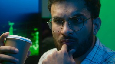 Yakın plan Hint Arap adam elinde kahve içerken düşünceli erkek programcı işçi tüccar serbest ticaret grafiği ev yapımı bilgisayar uzmanı gece çözümünü inceliyor.