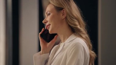 Eczane ilaç envanterinde cep telefonuyla konuşan beyaz kadın eczacı. Tıp önlüklü kadın. Akıllı telefon konuşuyor.