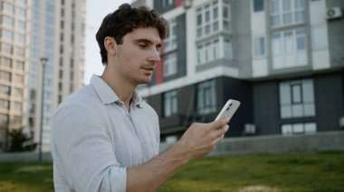 Kafkasyalı bir adam cep telefonu kullanıyor, akıllı telefon kullanıyor, sosyal medyada sohbet ediyor, internet üzerinden sohbet ediyor, gülümsüyor, uygulama yapıyor, erkek öğrenci aletleri, iş dünyası işadamı sokakta yürüyor, şehir dışına çıkıyor.