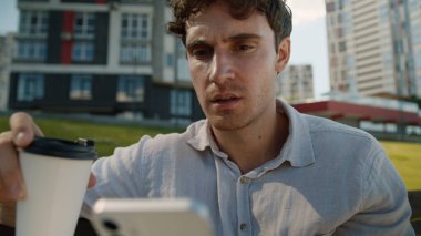 Kafası karışmış Kafası karışık beyaz adam cep telefonu kullanıyor. Akıllı telefon kullanıyor. Haber okuyan erkek öğrenci, kahve içiyor.