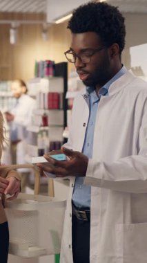 Eczacı doktor, eczane sağlık ürünlerindeki vitaminlerin satın alınmasına yardımcı olur. Afrikalı Amerikalı erkek, beyaz kadın eczane tıbbi konsültasyonu satın alır.