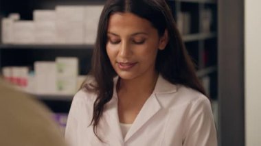 Eczanede müşteriyle konuşan Hintli kadın eczacı, kadın danışman hastaya reçeteli tıbbi danışmanlık, tıbbi danışmanlık, eczacılık, sağlık ve eczane satın alma gibi konularda gülümsüyor.