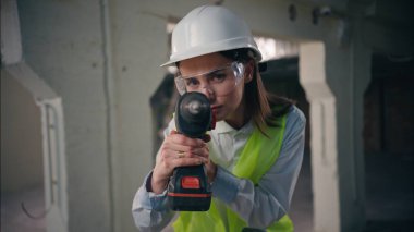 Kafkas kadın işçi inşaatçı kamera görüntüsüne bakıyor. Döner matkap onarımı. Kasklı yelek güvenlik gözlüğü takan güçlü kadın mühendis.