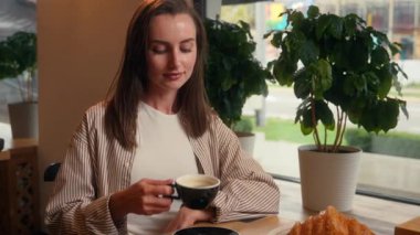 Kafeteryadaki masada oturan Kafkasyalı kadın kahve içiyor. Çay içiyor. Sabah kahvaltısı molası veriyor ve kameraya bakıp mutlu mesut gülümsüyor.