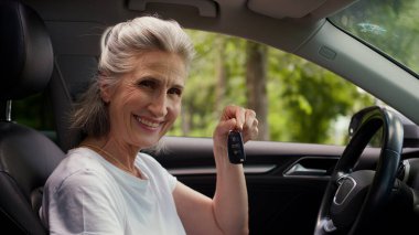 Neşeli, beyaz, yaşlı, yaşlı, gülümseyen, olgun bir kadın, otomobil şoförü, araba şoförü, araba anahtarı ve kredi kartını gösteren kameraya bakan, yeni bir araba kredisi satın alan,