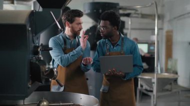 Kahve çekirdeği fabrikası değerlendirmesi. Kafkasyalı bir adam, Afrika kökenli Amerikalı meslektaşı konuşma örneğini incelerken, online veri toplama kalite değerlendirmesi yapıyor. İki küçük işletme sahipleri kapalı alanda küçük işletme sahiplerini tartışıyor.