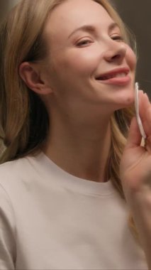 Elinde pamuk tutarak yüzünü temizleyen mutlu genç bir kadın. Tuvalette sağlıklı bir cilt. Kafkasyalı güzel bir bayan model.