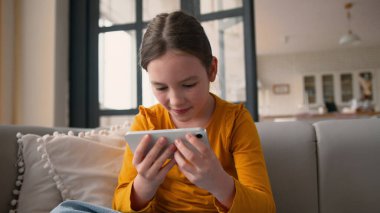 Neşeli, mutlu, beyaz bir çocuk cep telefonuna dokunuyor, akıllı telefon ekranı oynuyor, gülümsüyor, okulda zaferi kutluyor.