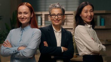 Üç kendine güvenen çok ırklı kadın iş yeri beyaz Asyalı meslektaşları kameraya bakıp gülümsüyor. Çok ırklı pozlar veriyor, el ele tutuşuyor, iş arkadaşları iş arkadaşları çeşitliliği gösteriyor.