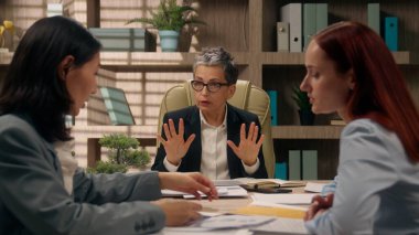 Takım çalışması, Kafkasyalı liderin Asyalı işçilere brifing vermesi, iş arkadaşlarının iş ortaklarıyla görüşmesi, iş kadınlarının iç mekanda iş birliği yapması.