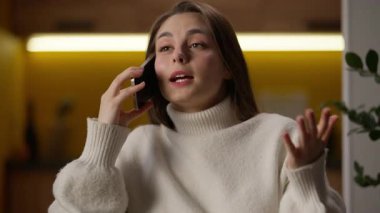 Kafkasyalı kadın cep telefonuyla konuşuyor duygusal kadın dedikoducu, güler yüzlü iletişim kızı ev hanımına oturma odasında iyi haberleri paylaştığını söylüyor.