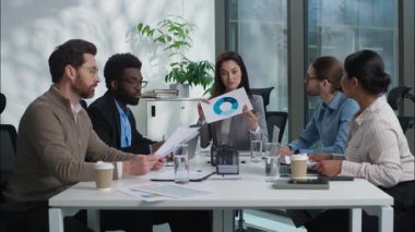 Beyaz iş kadını takım lideri grafik çizelgesi gösteriyor. İki çok ırklı iş adamı tokalaşıyor. El sıkışıyorlar.