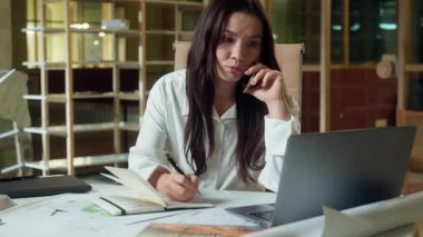 Asyalı iş kadını organizatör kadın iş kadını konuşan cep telefonu danışmanı müşteri online iş bilgisayarı ofisinde Çinli Koreli Japon kız not defteri yazıyor.