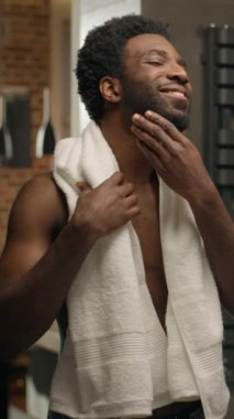 Afro-Amerikalı çıplak adam, aynada gülümseyen sakallı erkek adam, sabah tıraş oluyor, duş alıyor, yüzünü tıraş ediyor, cildini tıraş ediyor, makyaj yapıyor, losyon kremini nemlendiriyor.