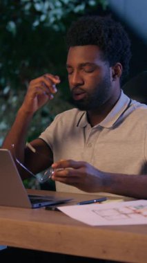 Afro-Amerikalı mimar dizüstü bilgisayar, gece vardiyasında fazla mesai yapıyor. Yorgun iş adamı, yorgun, yorgun, erkek adam rahatsız. Gözlüklerini çıkarıyor.