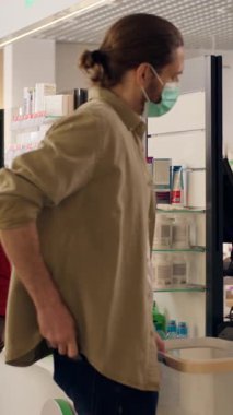 Maske eczanesindeki çeşitli müşteriler antiviral ilaç satın alıyor. Enfeksiyon enfeksiyonu olan eczacı kadın, hastalara sağlık hizmetleri için ilaç paketlemede, ilaç paketlemede, kredi kartı ödeme dükkanında yardım ediyor.