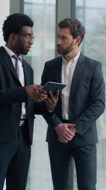 Modern ofiste projeyi tartışan iki çok ırklı iş adamı dijital tablete bakıyorlar çok ırklı iş adamları çeşitli erkek iş arkadaşları iş birliği stratejisi planlama hakkında konuşuyorlar.