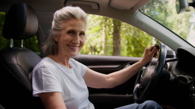 Gülümseyen, emekli, Kafkasyalı, mutlu, yaşlı, emekli kadın, kadın, araba şoförü, arabada oturan, kameraya gülümseyen, el ele tutuşan, direksiyon sallayan, emekliliğe giden kadın.