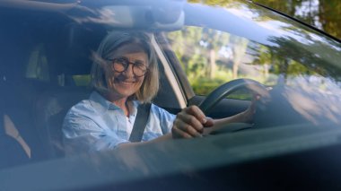 Başarılı, beyaz, gülümseyen yaşlı iş kadını olgun, kadın, iş kadını, araba şoförü, kiralık müşteri yeni aracın içinde oturuyor emniyet kemeri takıyor kamera görüntülü gülümseme.