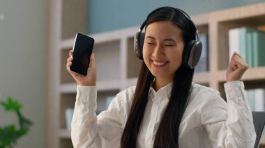 Neşeli öğrenci Asyalı Koreli kadın iş kadını Japon işkadını ofis çalışanı cep telefonu akıllı telefon uygulaması kullanıyor içeriden müzik kulaklığı dinliyor