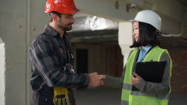 Çok uluslu odaklı mühendisler projesi, el sıkışma, el sıkışma, Asyalı kadın, beyaz şapkalı adam, pano inşaat sahası ortaklığı, takım çalışması mimarisi konularına dikkat çekiyor.