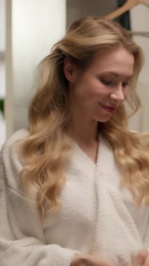 Güzel, beyaz bir kadın, banyo mankeni bornozunda saçlarını tarıyor, saçlarını tarıyor, saçlarını tarıyor. Ev banyosunda güzellik şampuanı kreminin keyfini çıkarıyor.