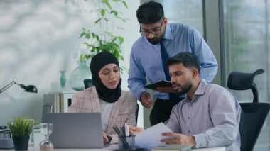 Üç Hint Arap iş adamı ofiste proje stratejisini tartışıyor mali raporları inceliyor dizüstü bilgisayarlara bakıyor fikir alışverişi yapıyor şirket toplantıları yapıyor.