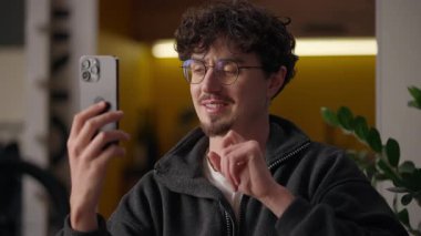 Gülümseyen İspanyol adam hipster cep telefonuyla konuşuyor. Neşeli erkek evde sohbet ediyor. İnternetteki adam sanal konferansında uzaktan iletişim uygulamaları ile konuşuyor.