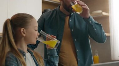 Kafkasyalı mutlu aile fertleri sabah evde, mutfakta baba ve küçük kız çocuk taze turunçgil vitamini portakal suyu içiyorlar baba dizüstü bilgisayarlı çocuğun birlikte takılmasına yardım ediyor.