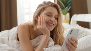 Gülümseyen Kafkasyalı kadın cep telefonunu kaydırarak kazanıyor neşeli kız, akıllı telefon mesajı yazıyor iyi haber başarısı kadın şokunu kazanan kadın şokunu yaşıyor.