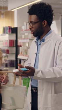 Afro-Amerikalı erkek eczacı, eczane doktorundan ilaç alan, ilaç siparişi veren, ilaç sipariş eden, ilaç alan, beyaz kadın müşterilere danışmanlık yapıyor.