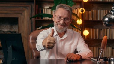 Kendinden emin, yaşlı, beyaz, olgun bir erkek kamera önünde el ele tutuşmuş ofis işadamı yakışıklı, yaşlı çalışan portresi liderinin içindeki iş adamına bakıyor.