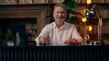 Kendinden emin, yaşlı, beyaz, olgun bir erkek kamera önünde el ele tutuşmuş ofis işadamı yakışıklı, yaşlı çalışan portresi liderinin içindeki iş adamına bakıyor.