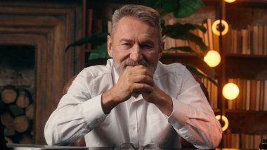 Kendinden emin, yaşlı, beyaz, olgun bir erkek kamera önünde el ele tutuşmuş ofis işadamı yakışıklı, yaşlı çalışan portresi liderinin içindeki iş adamına bakıyor.