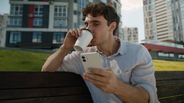 Kafası karışmış Kafası karışık beyaz adam cep telefonu kullanıyor. Akıllı telefon kullanıyor. Haber okuyan erkek öğrenci, kahve içiyor.