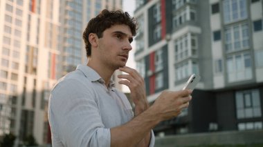 Kafkasyalı bir adam cep telefonu kullanıyor, akıllı telefon kullanıyor, sosyal medyada sohbet ediyor, internet üzerinden sohbet ediyor, gülümsüyor, uygulama yapıyor, erkek öğrenci aletleri, iş dünyası işadamı sokakta yürüyor, şehir dışına çıkıyor.