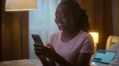 Neşeli Afrikalı Amerikalı etnik iş kadını kadın iş kadını cep telefonu düşünen cevap veren internetteki yazışmalara cevap veren internet uygulaması evde dizüstü bilgisayarda oturup mesajlaşan mesajlar yolluyor.