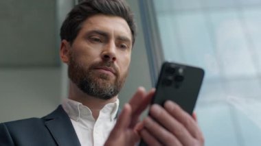 Sakin Kafkas 'lı 40' lı yılların işadamı ofiste cep telefonu kullanıyor. Pencereden dışarı bakıyor. Erkek girişimci, dalgın iş adamı internette akıllı telefonlardan sohbet ediyor.