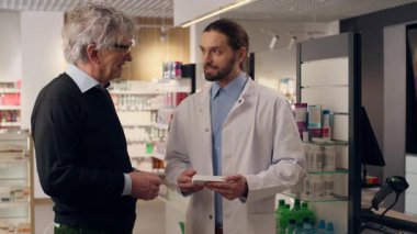 Olgun, yaşlı bir eczacı eczaneden ilaç almaya yardım ediyor. Kalp hapları, sağlıklı vitaminler, güler yüzlü erkekler. Müşterinin sağlık hizmetlerine yardım eden doktor.