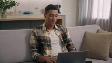 Neşeli, kaygısız, gülümseyen Afrikalı Amerikalı adam internet işiyle meşgul. Ev bilgisayarında uzak internet işi yapıyor. Bilgisayarlı, bilgisayarlı, e-öğrenen bir adam.