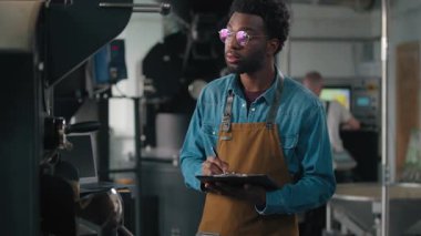 Küçük işletme sahibi Afro-Amerikan erkek adam kavrulmuş kumaş kalite kavrulma makinası kontrol fasulye yöneticisi inceleme süreci denetleme belge teftişinde notlar yazma