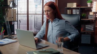 Beyaz iş kadını ofiste dizüstü bilgisayarda yazı yazıyor. Sırt ağrısı çekiyor. Aşırı çalışma, aşırı çalışma, hasta, rahatsız edici sırt ağrısı.